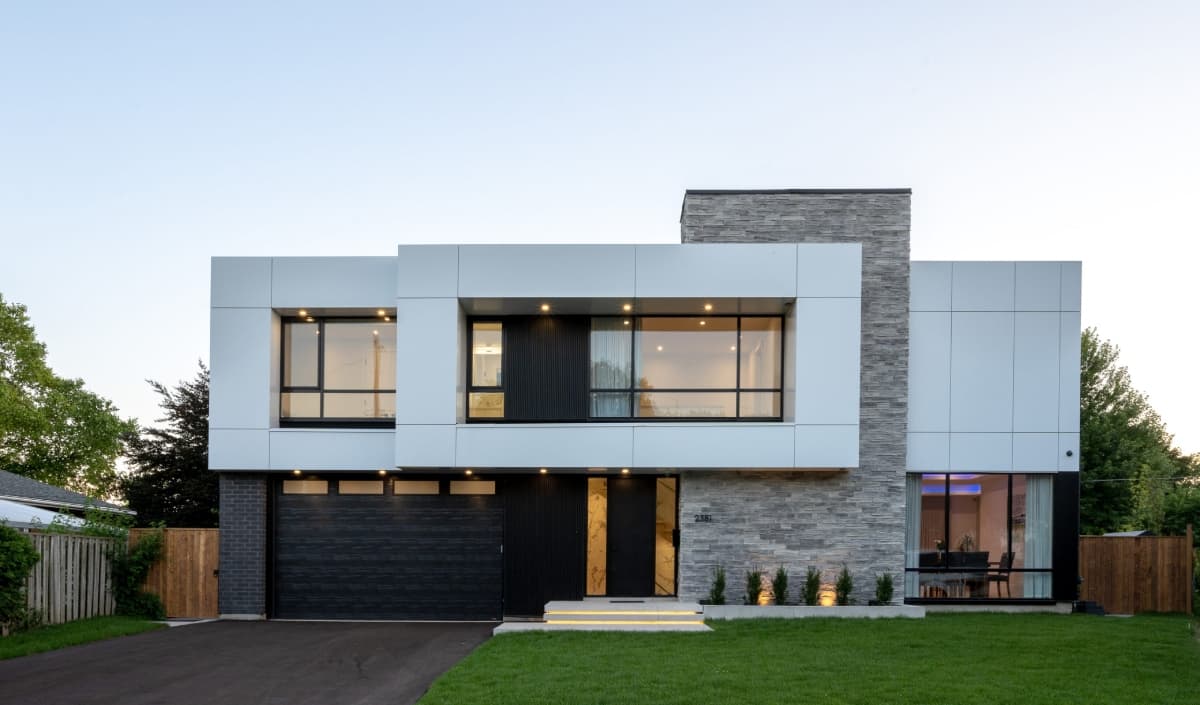 A modern custom home designed by Lima Architects, with white volumes, stone cladding and glazing lit at dusk